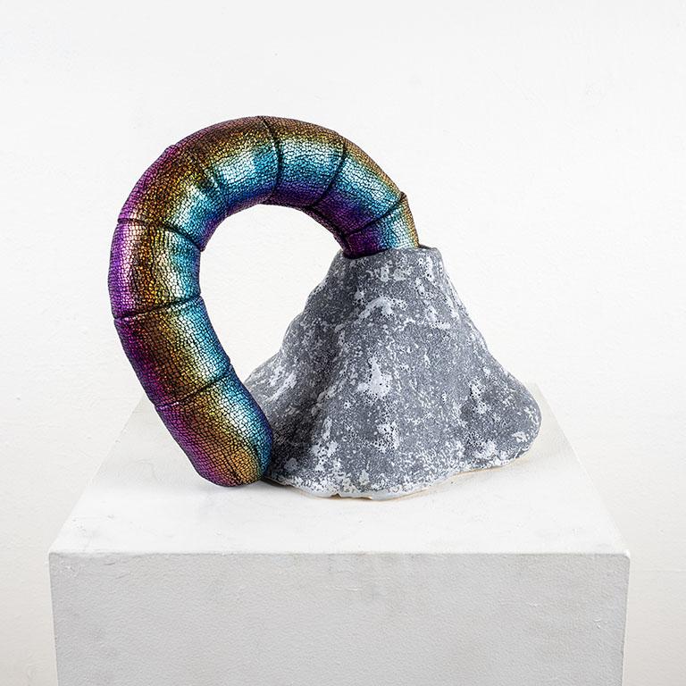 Wrapped metallic multicolored worm figure coming out of a stone cast hill.