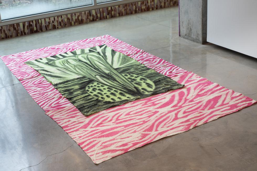 A bright pink and off-white zebra print textile laying on a concrete floor with a light and dark green textile with an abstract designlaid over it.