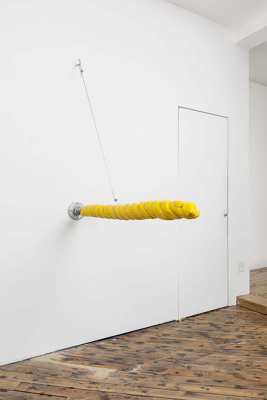 Yellow swirled pole sticking out of a wall held up by a cable against a white wall with wooden floors.