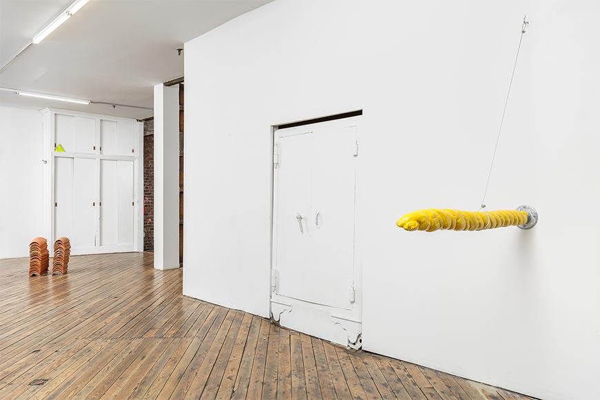 White room with wooden floors, yellow swirled object sticking out of the wall to the right with ceramic tiles in the background.