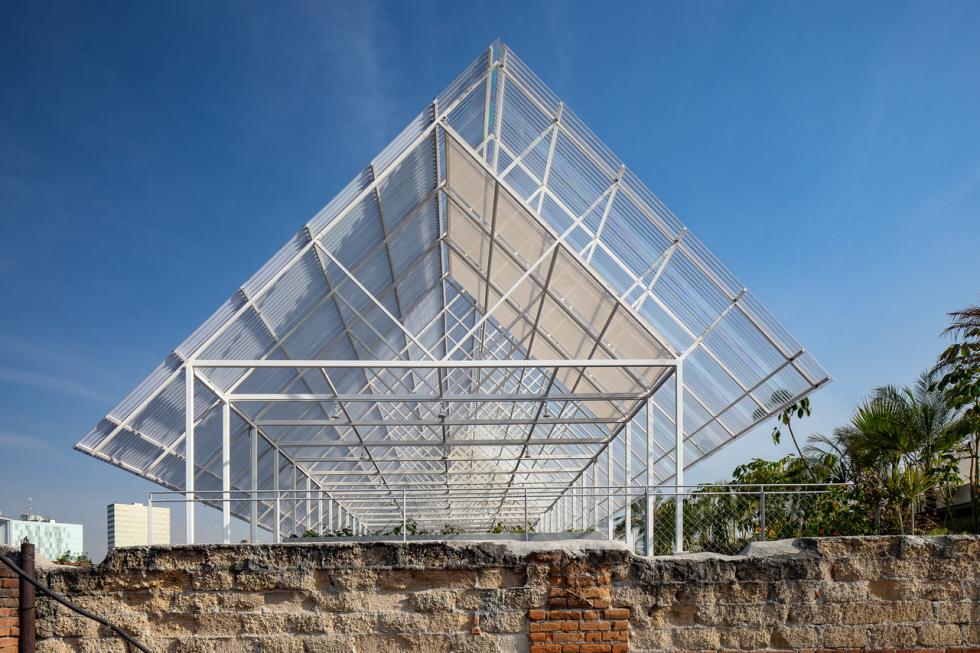 A large building featuring glass walls, set against a backdrop of the sky with clouds, resembling a greenhouse.