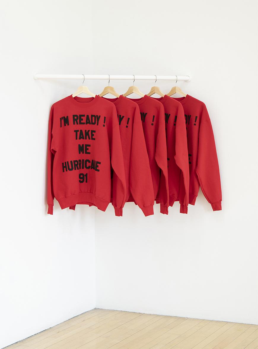 Five red sweatshirts hanging on a white rod with the words 