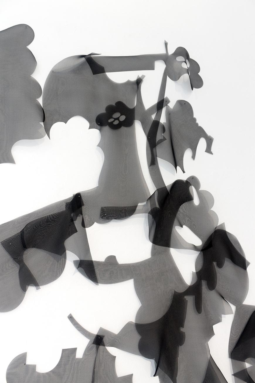 Vertical photo of black transparent abstract shapes against a white wall