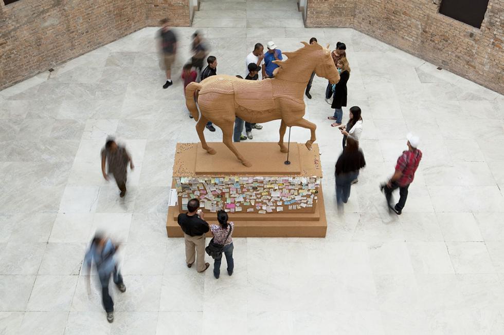 Statue of a horse made of cork, pushpins, notes contributed by the public with people walking around it.