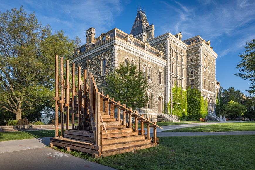 A picture of wooden stairs on the grass with a brick building in the background