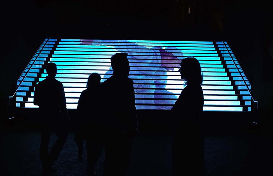 Silhouetted figures backlit by the image of personthrowing a ball.