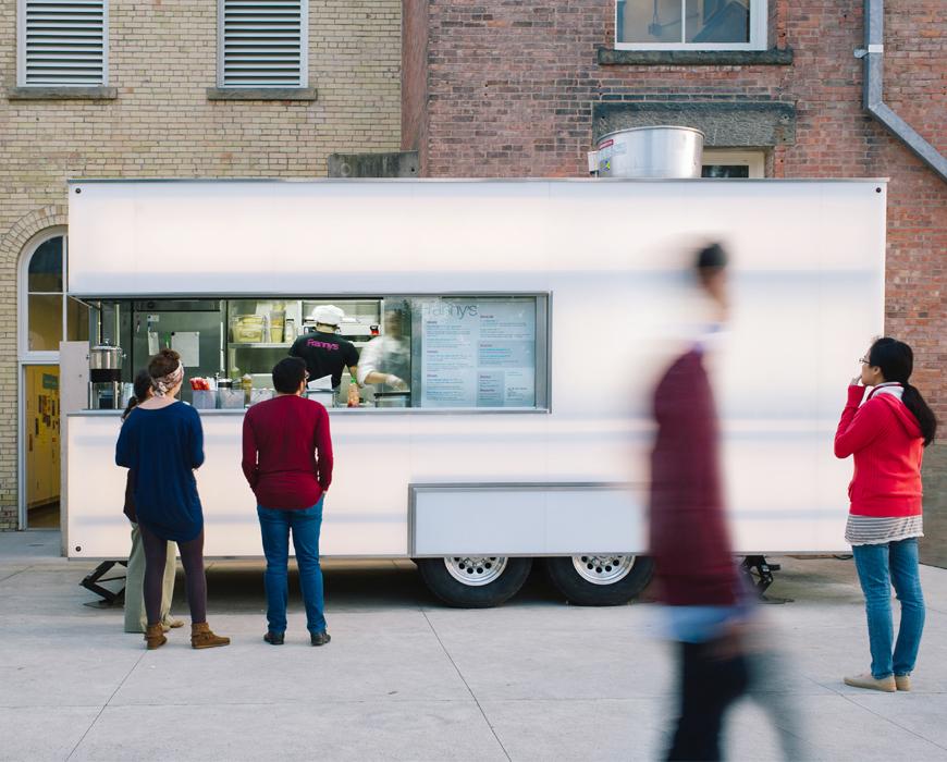 A picture of a modern, lit up food truck in front of brick buildings