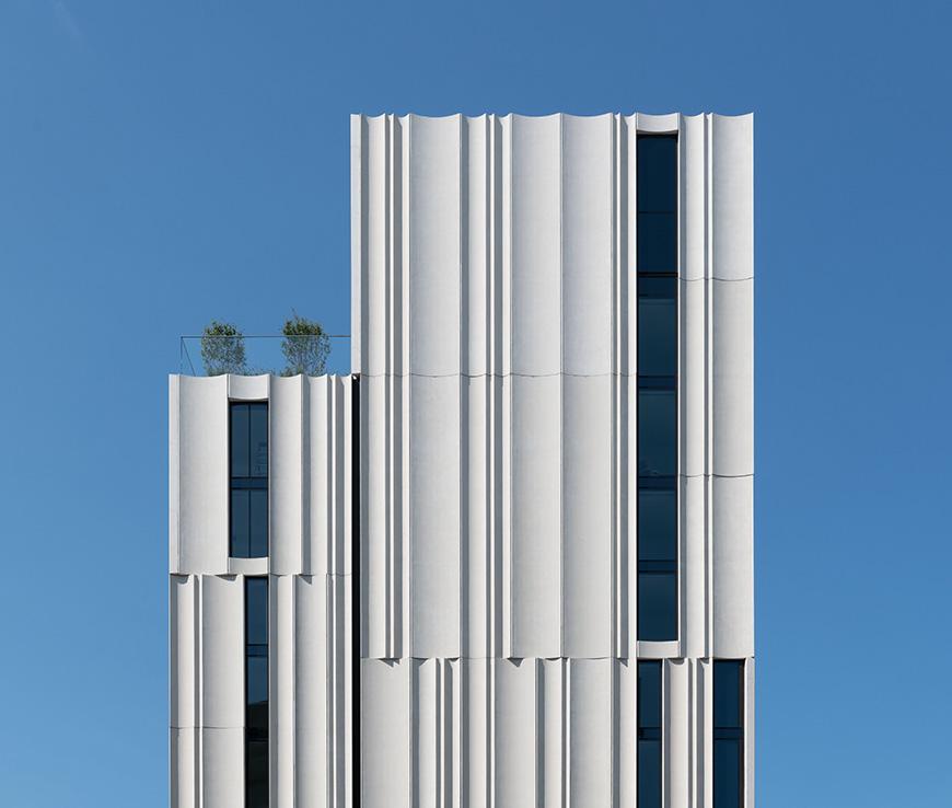 facade of upper floors of a white fluted high-rise building against blue sky