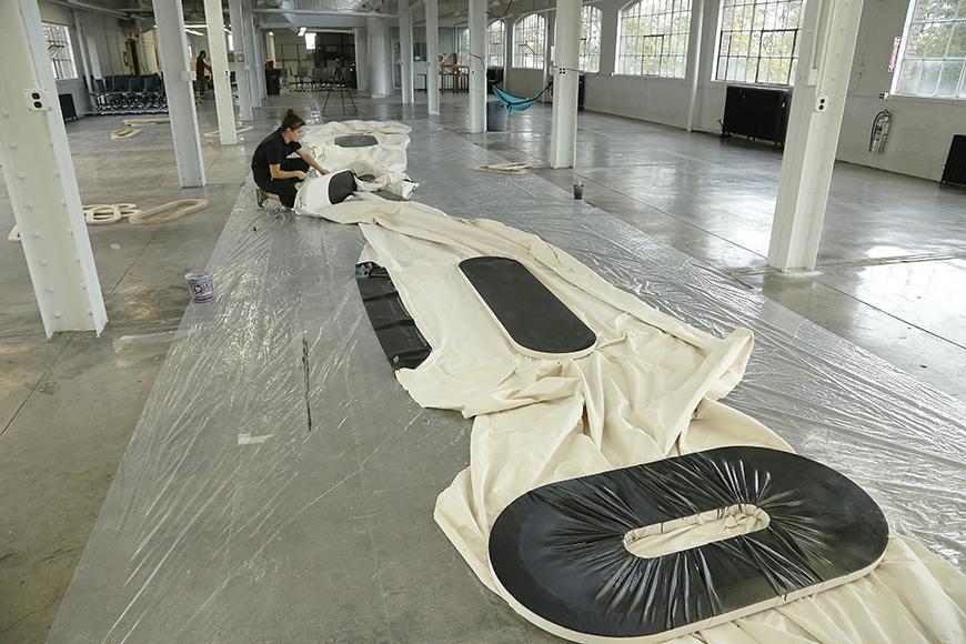 Artist laying down white cloth with black oblong shapes painted on it on the floor.