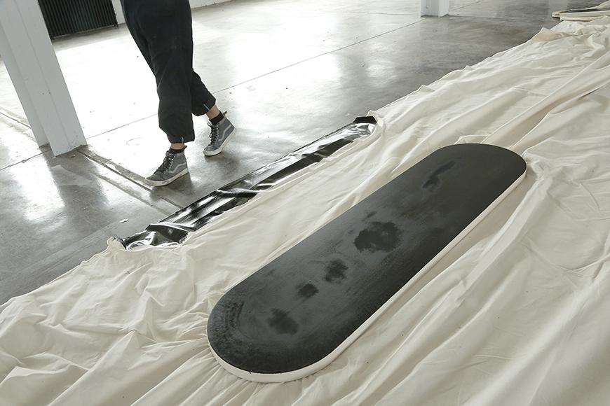 Artist walking around white cloth taped to the floor with a black oblong shape in the middle.