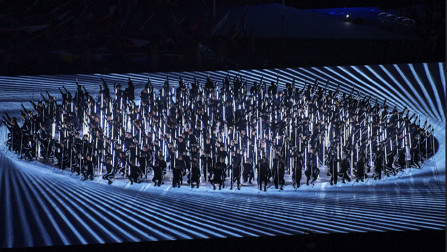 A large group of people standing in a circle and surrounded by light effects in a performance.