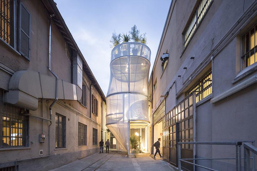 An alley between two concrete buildings with a lit tower structure in the center.