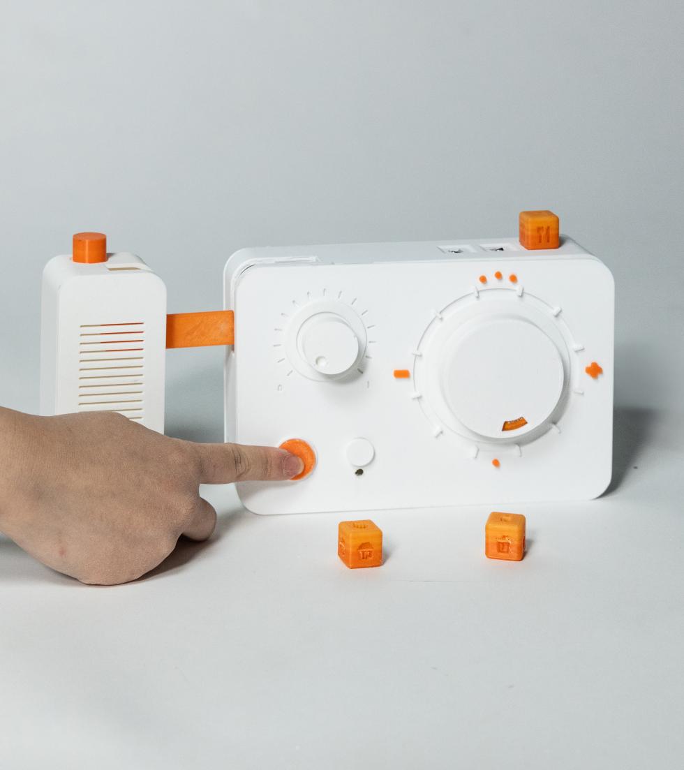 A hand operating a rectangular device with buttons, rotationg knobs, and small cubic attachable pieces.