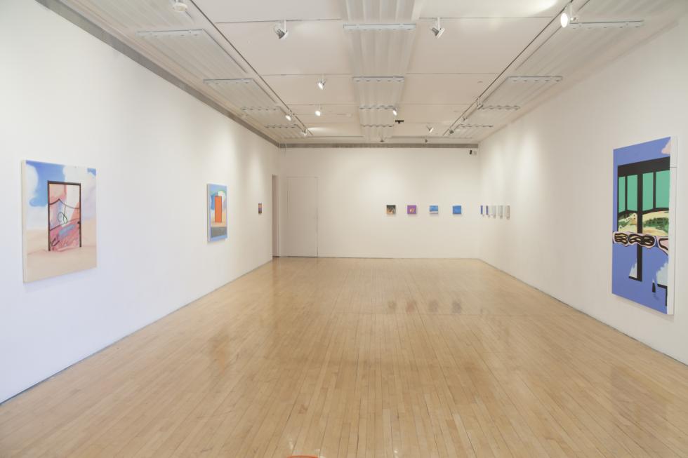 Installation view of paintings exhibited in a long white room with wooden floors.