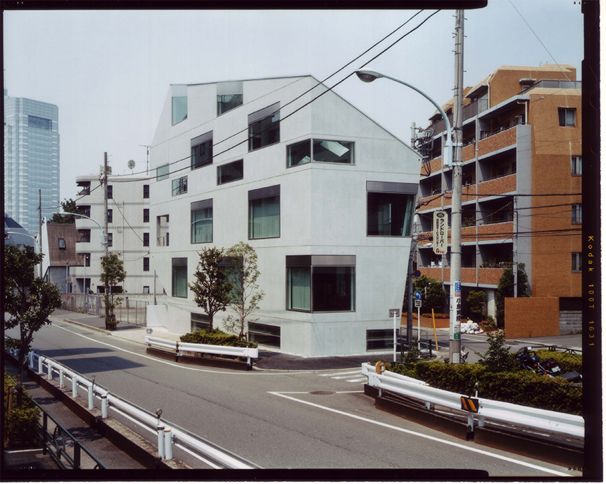 Modern white 4-story building whose facade consists of a series of interspersed square and rectangular windows.  