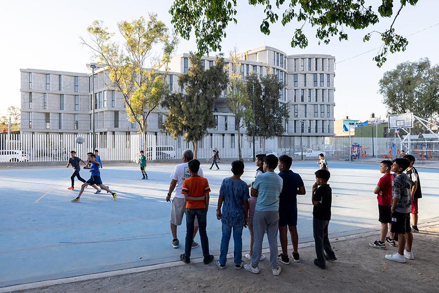 Childredn playing sports on a playground, apartment-style building in background.