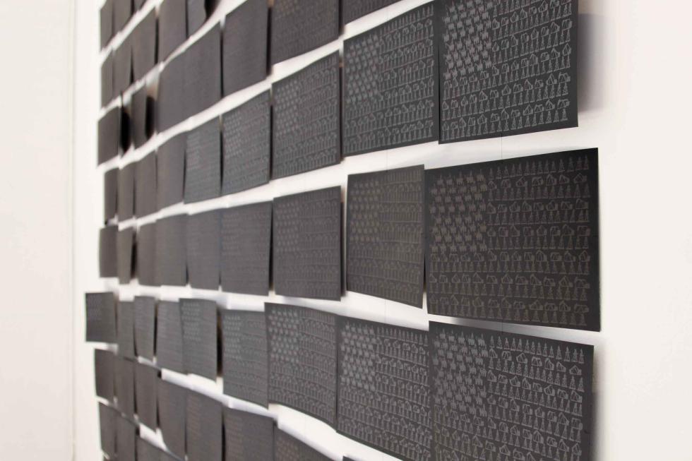 Black rectangular prints with metallic ink arranged in a pattern on a white wall.