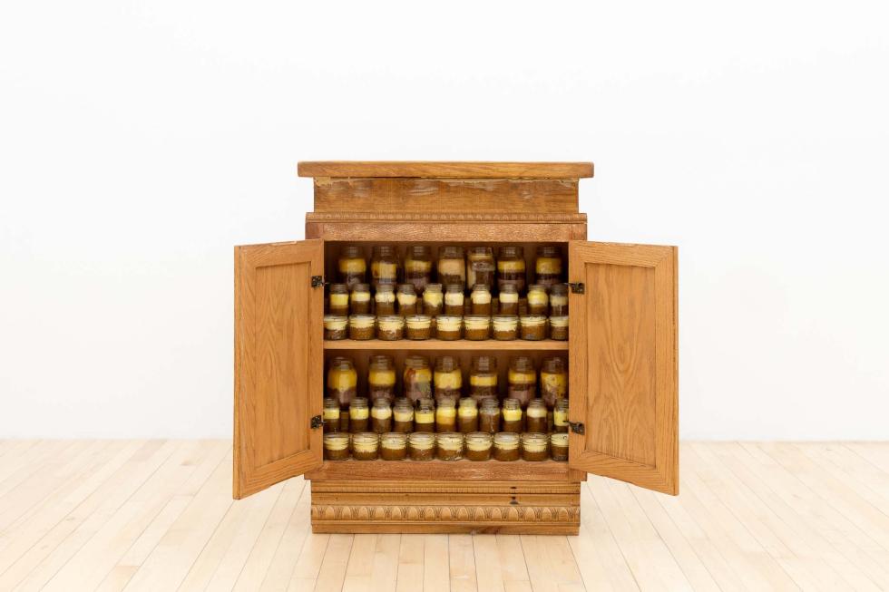 Open wooden cabinet with many jars of beeswax and miscellaneous materies.
