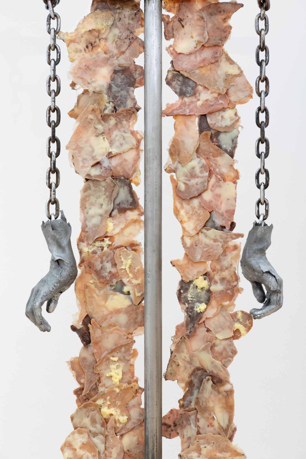 Steel pole with two steel casted hands hanging on either side on a chain with silicone chicken skins draped around it.