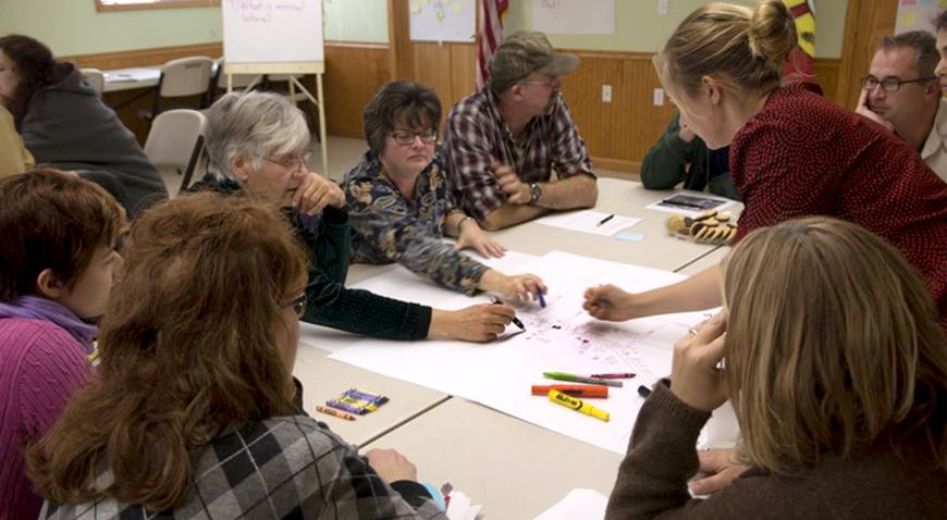 people gathered around a desk working on a project involving paper and markers