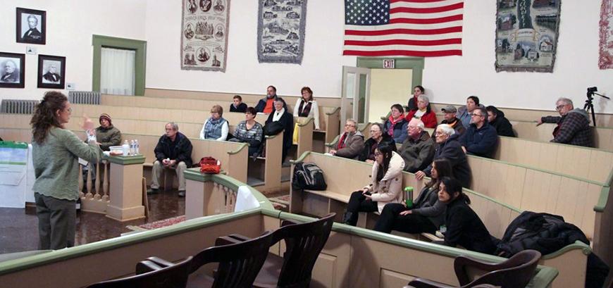 people gathered in what a court room with an American flag hung on the wall and other framed photographs