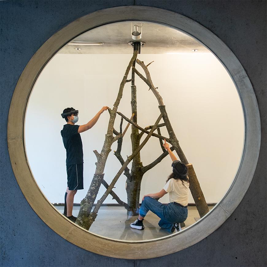 two people building a structure out of logs, viewed through a window