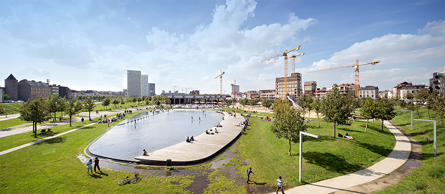 Landscape of a park centered around an artificial pond within a cityscape. 