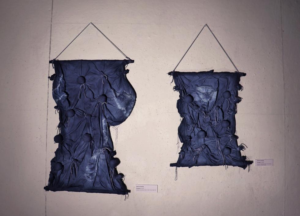 Two pieces of dark purple fabric with bunched up pieces hung from the wall.