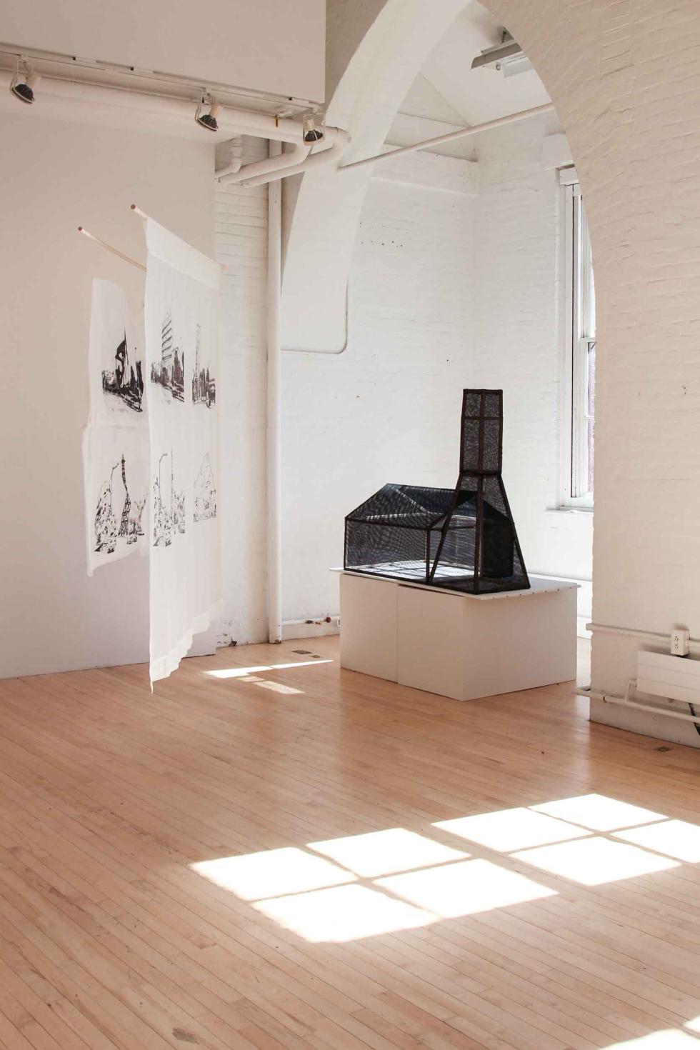 Two white banners with four black images printed on them hanging next to a black transparent building model in a white room.