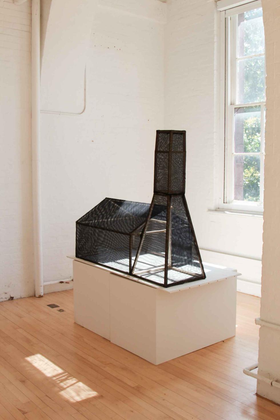 A black transparent building model in a white room next to a window.