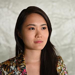 A woman with long black hair, wearing a multicolored pattered shirt. 