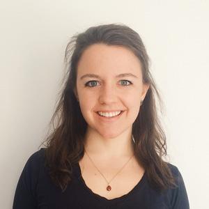 headshot of a young woman with brown hair wearing a black shirt standing in front of a white wall