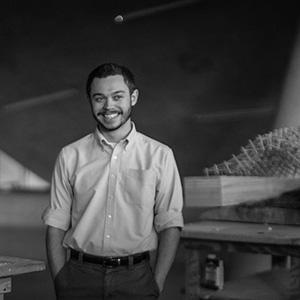 Black and White portrait of a young man with short hair and a beard, who is wearing a button up shirt. 