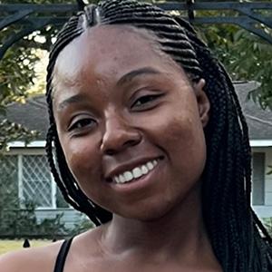 A smiling woman with dark skin and black hair worn in many small braids.