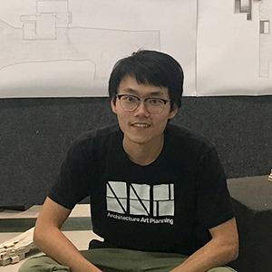 A man with glasses and a black t-shirt sitting.