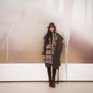 portrait of a woman from a distance wearing a hat standing in front of a brown and white wall