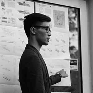 profile of the torso and head of a young man with dark and glasses standing in front of a diagram