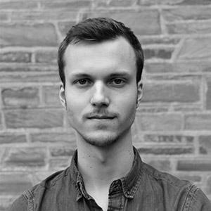 A black and white portrait of a man with short hair, who is wearing a button up shirt. 