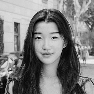 black and white headshot of a young woman with black hair and a building behind her