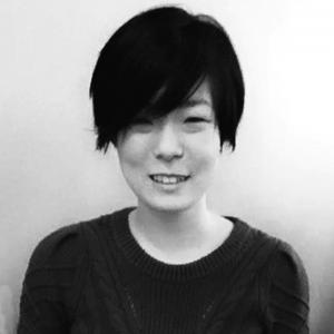 black and white headshot of a young woman with short dark hair wearing a black sweater standing in front of a white wall