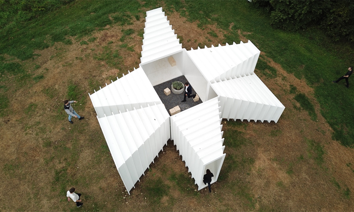 white geometric pavilion with multiple doorways and people around and inside