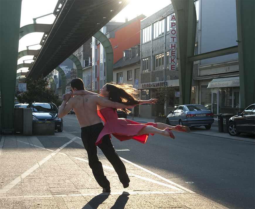 Two individuals dancing in the sunlight of a cityscape.