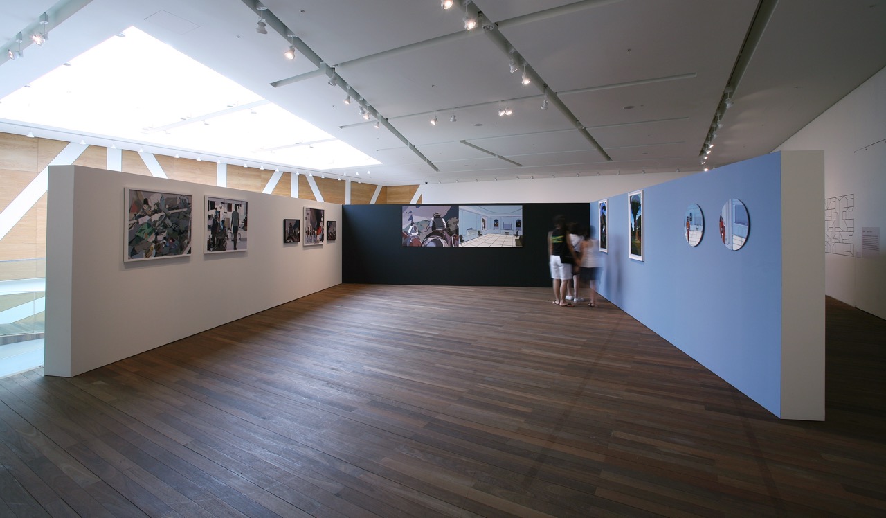 Three gallery walls, painted white, black, and blue, feature large scale mounted framed photographs with three gallery visitors viewing the artwork