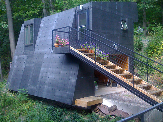 A dark colored metal clad contemporary tiny house with an angled wall and set of stairs on the outside.
