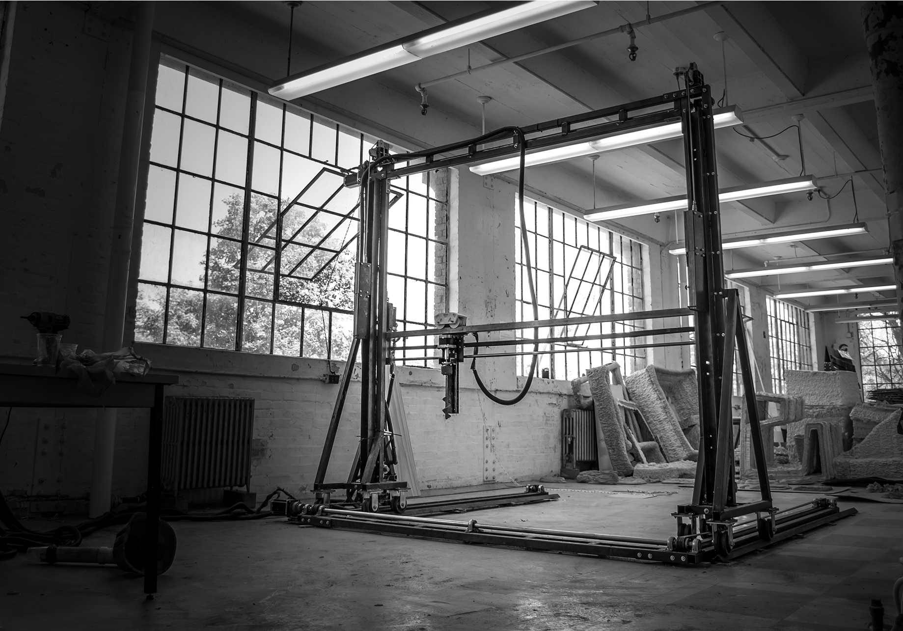 Black and white photograph of an upright robotic machine sitting in a building with large square windows.