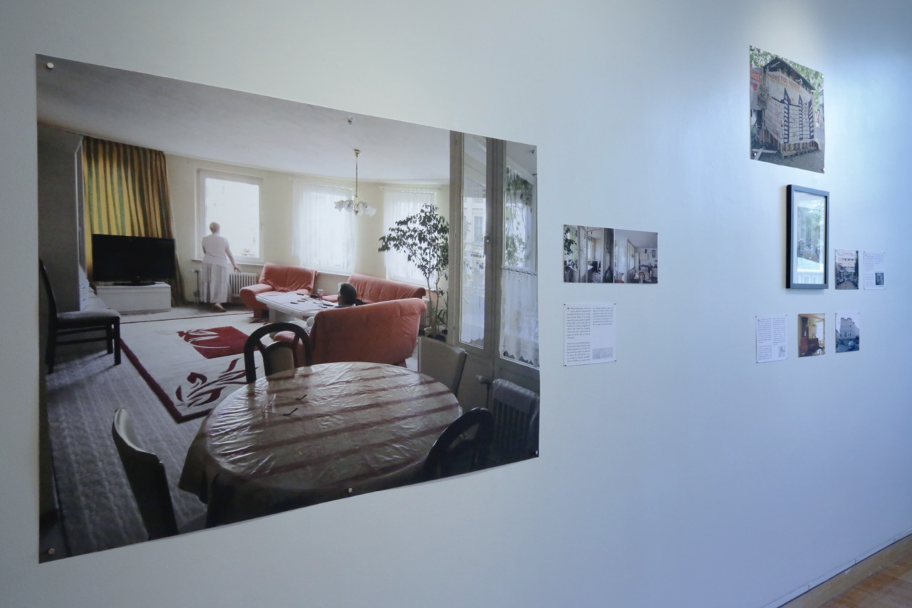 Photographs are pinned to a gallery wall depicting the interior of a home