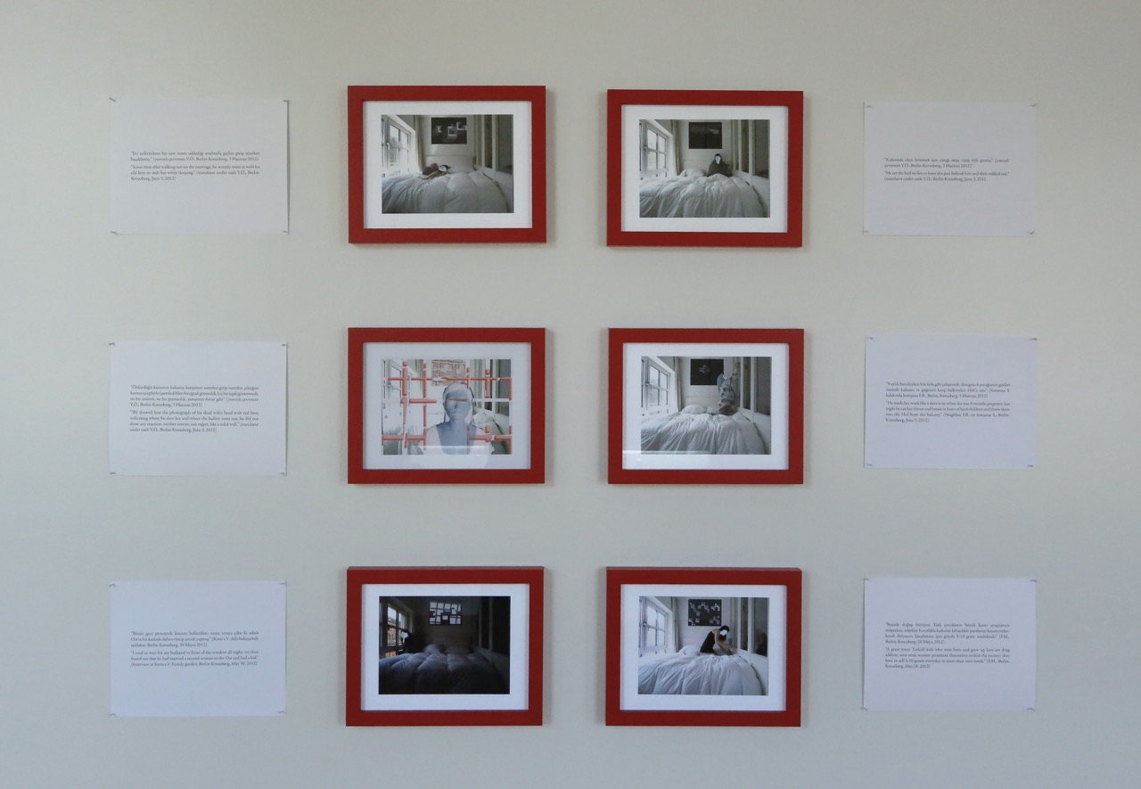 Six red-framed photographs are arranged in a grid on a gallery wall with caption cards for each photograph