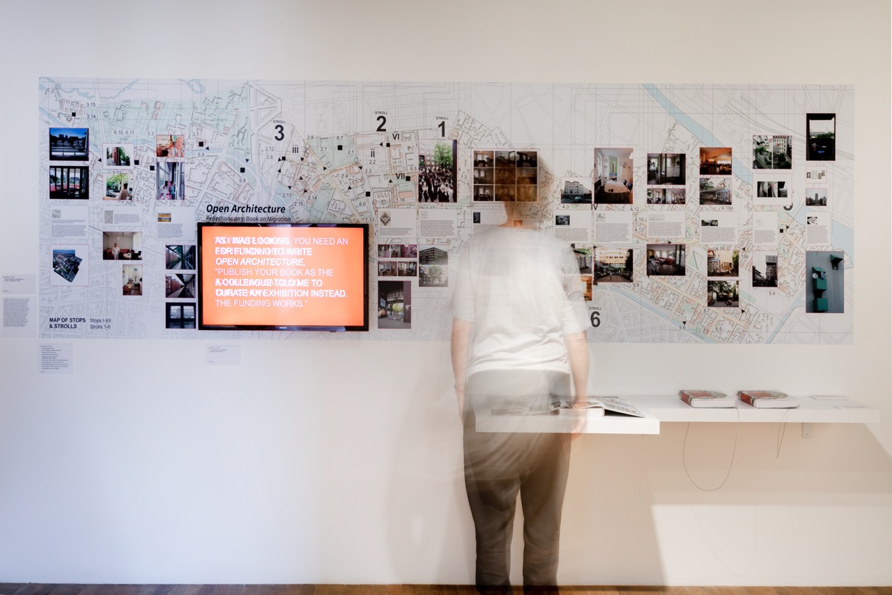 a person stands in front of a large infographic with a city map and photos on a gallery wall