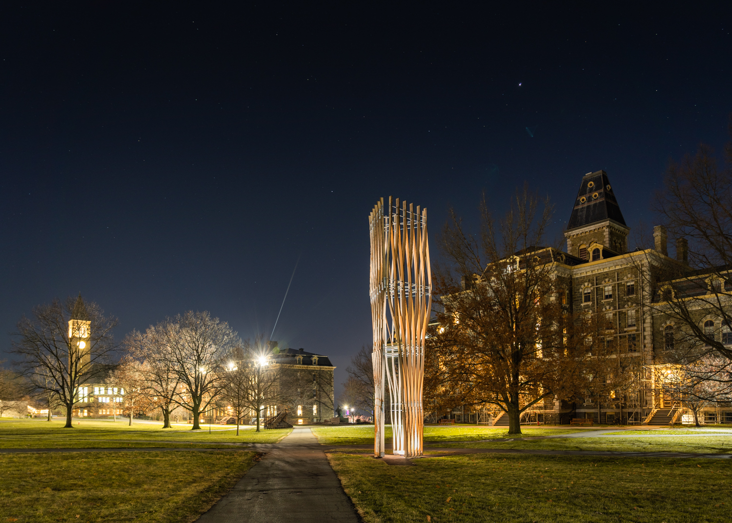 Wood and metal tower constructed on the grass in an open area surrounded by buildings on Cornell University campus.