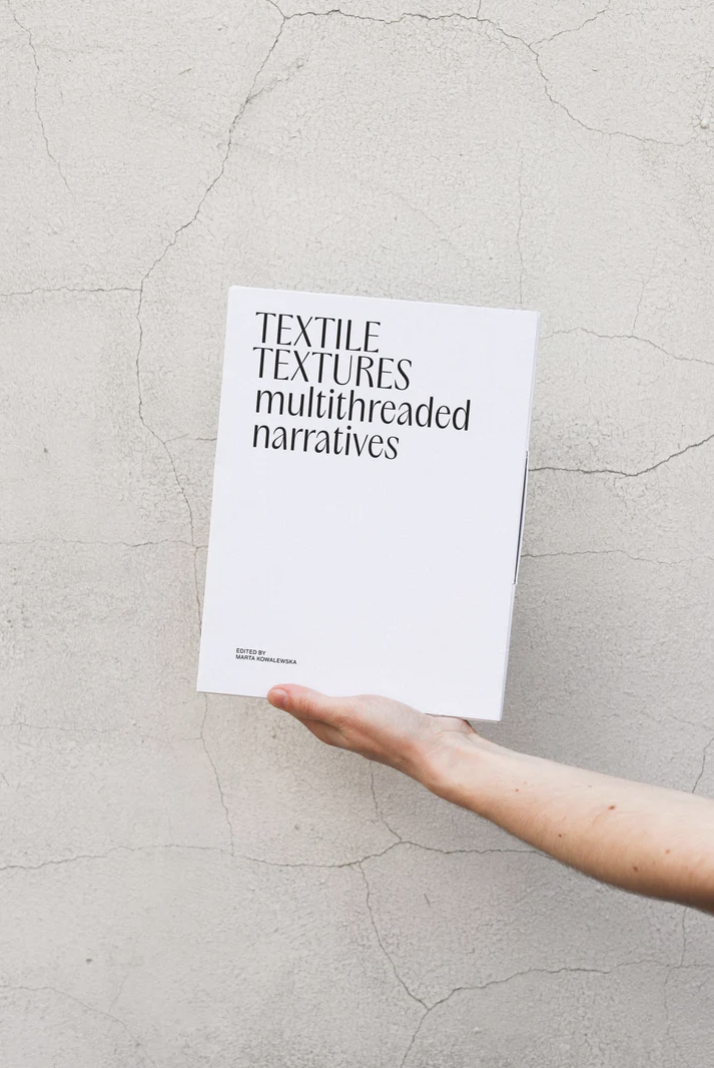 Person holding a white book with large black lettering on a beige marble background